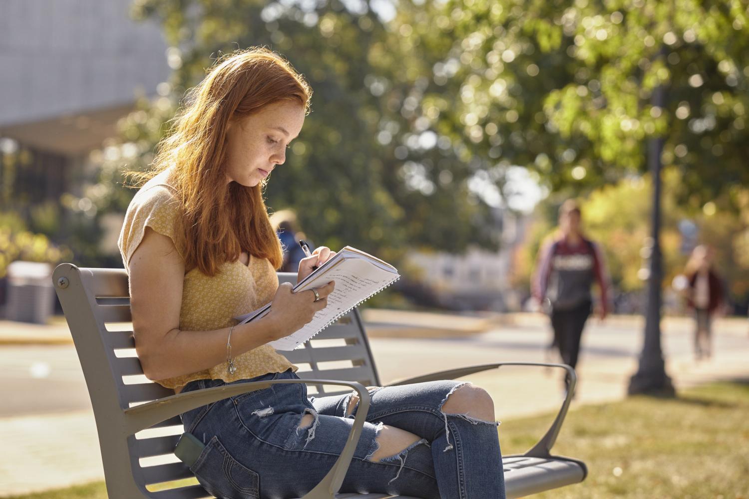 A <a href='http://79xg.jinken-fukuoka.com'>博彩网址大全</a> student reads on a bench along Campus Drive.